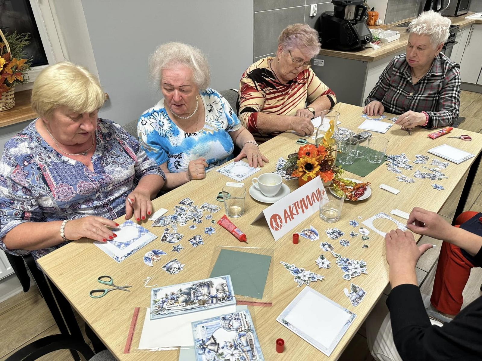 Kobiety siedzą przy stole robia kartki świąteczne 