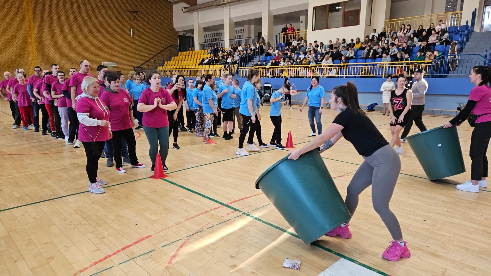 grupa os&oacute;b na hali, podzielonych na drużyny, jedna w r&oacute;żowych koszulkach, druga w niebieskich koszulkach