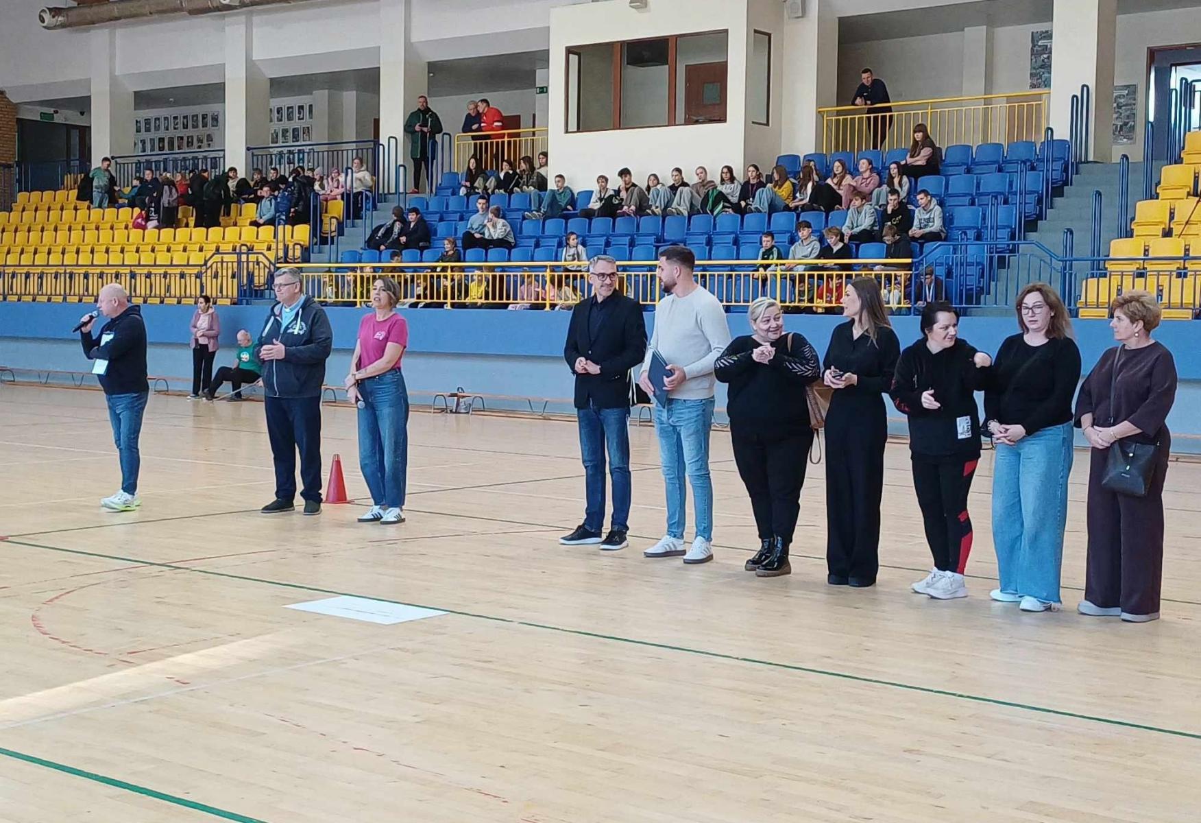 Goście i organizatorzy stoją na hali. 