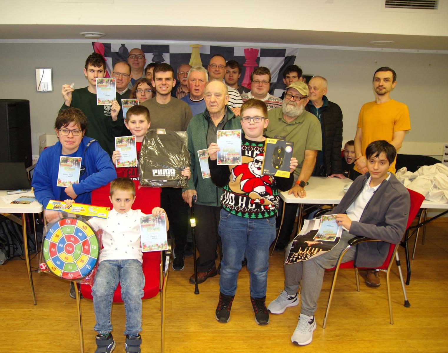 Grupa dzieci i dosrłych stoi w sali z dyplomami i prezentami 