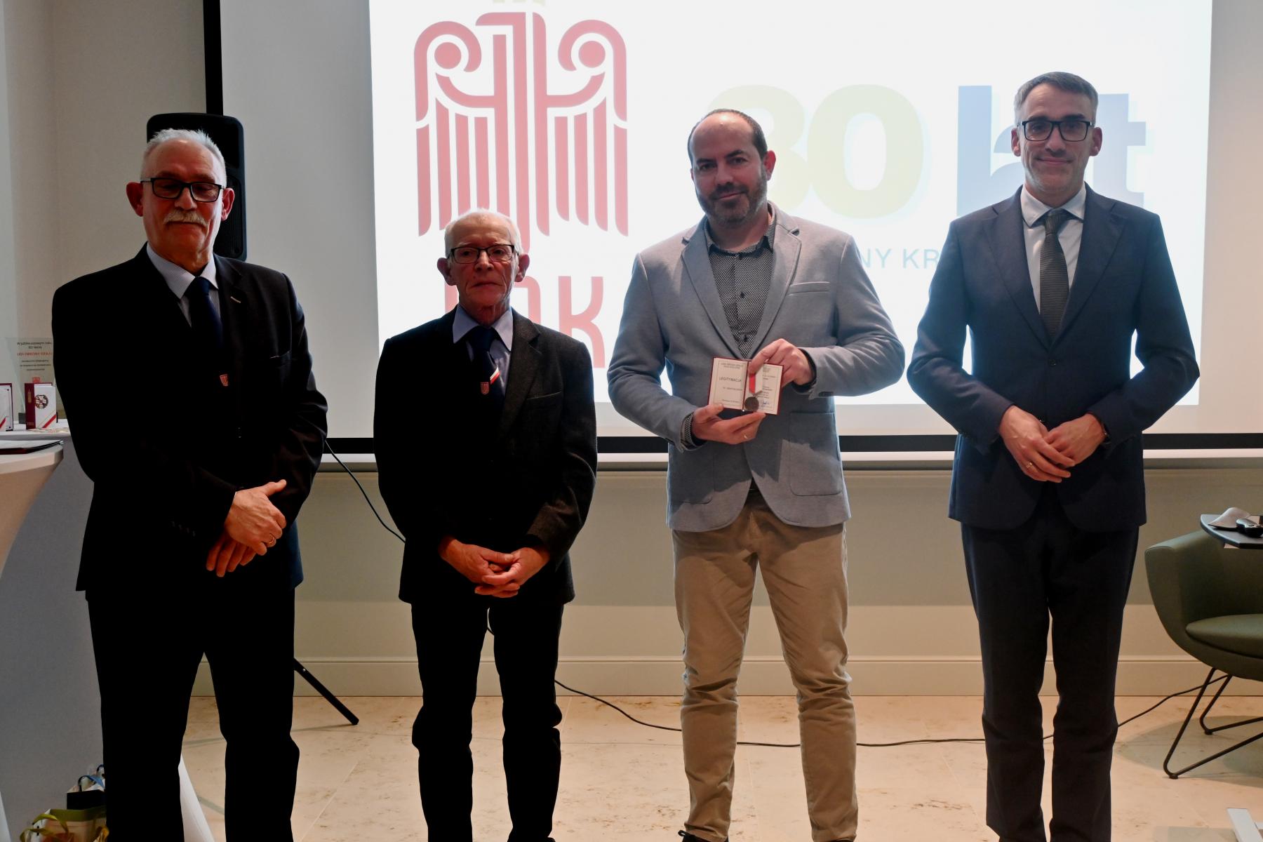 Czterech mężczyzn stoi w sali, w tle wyświetla się logo LOk i napis 80 lat