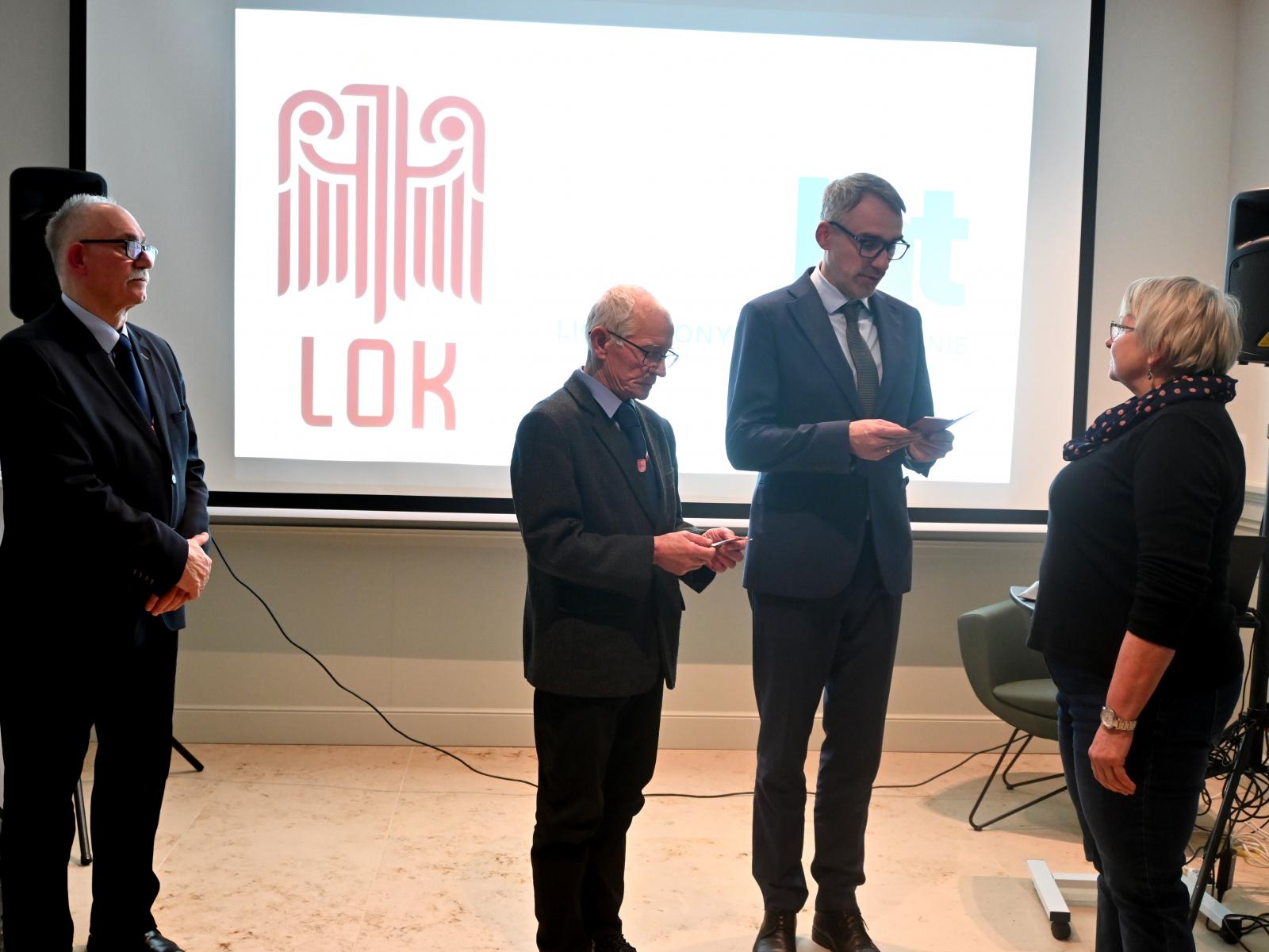 Od lewej stoją w sali: trzech mężczyzn i kobieta