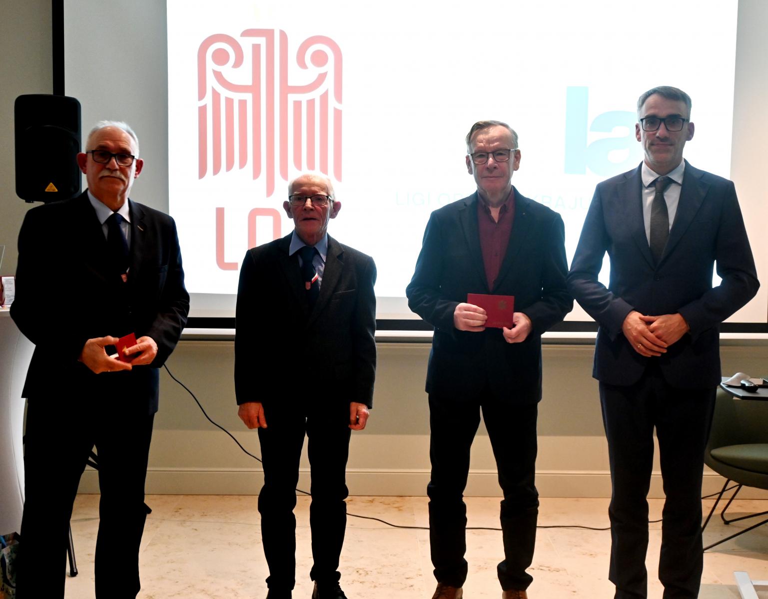 Czterech mężczyzn stoi w sali, w tle wyświetla się logo LOk i 80 lat