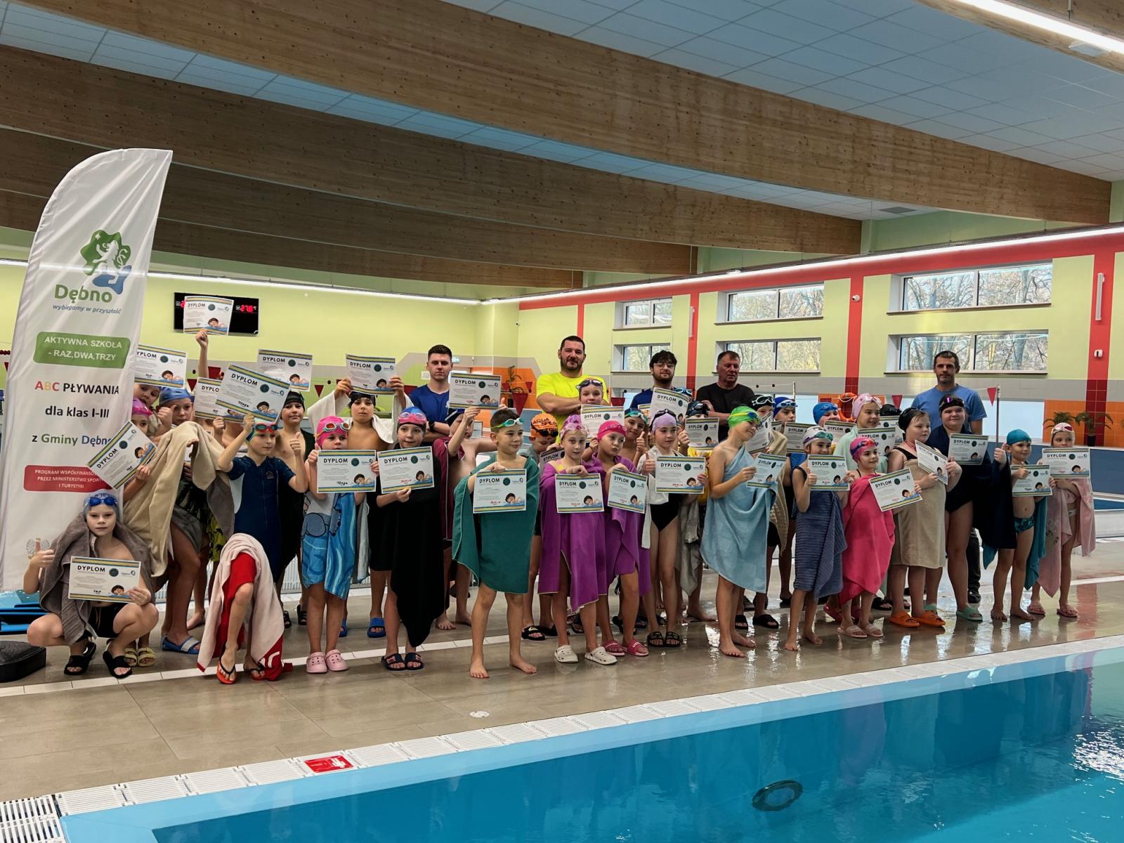 Grupa kilkunastu dzieci na basenie, trzymają dyplomy 
