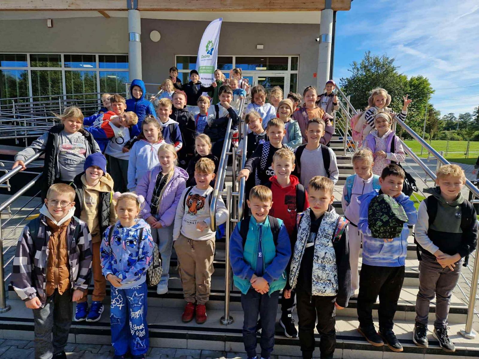 Ponad dwadzieścioro dzieci stoi przed budynkiem na zewnątrz