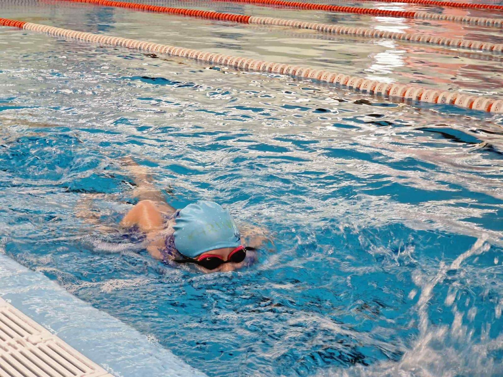 Dziecko w czepku i okularach pływackich pływa w basenie 