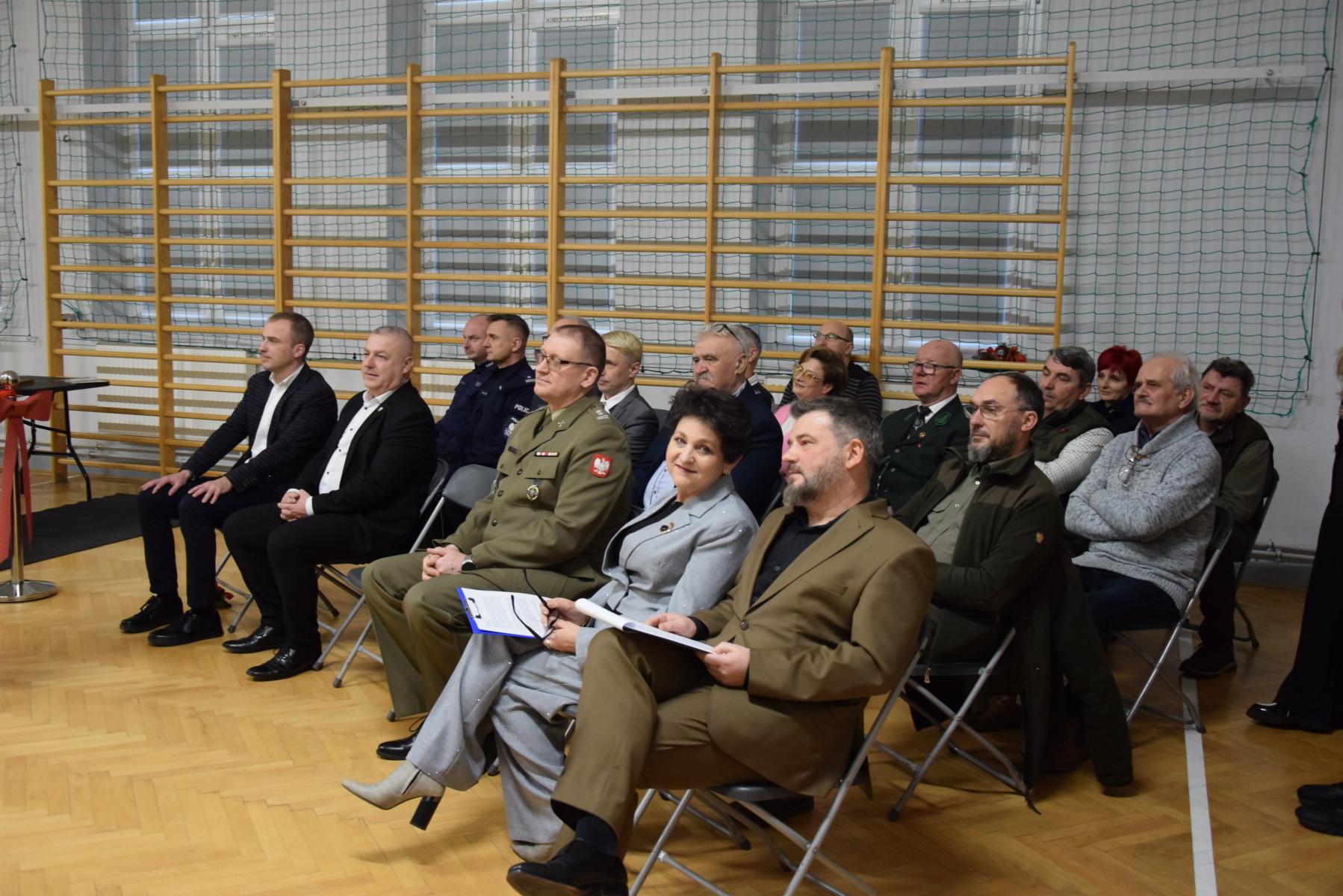 Grupa gości siedzą na krzesełkach w sali gimnastycznej 