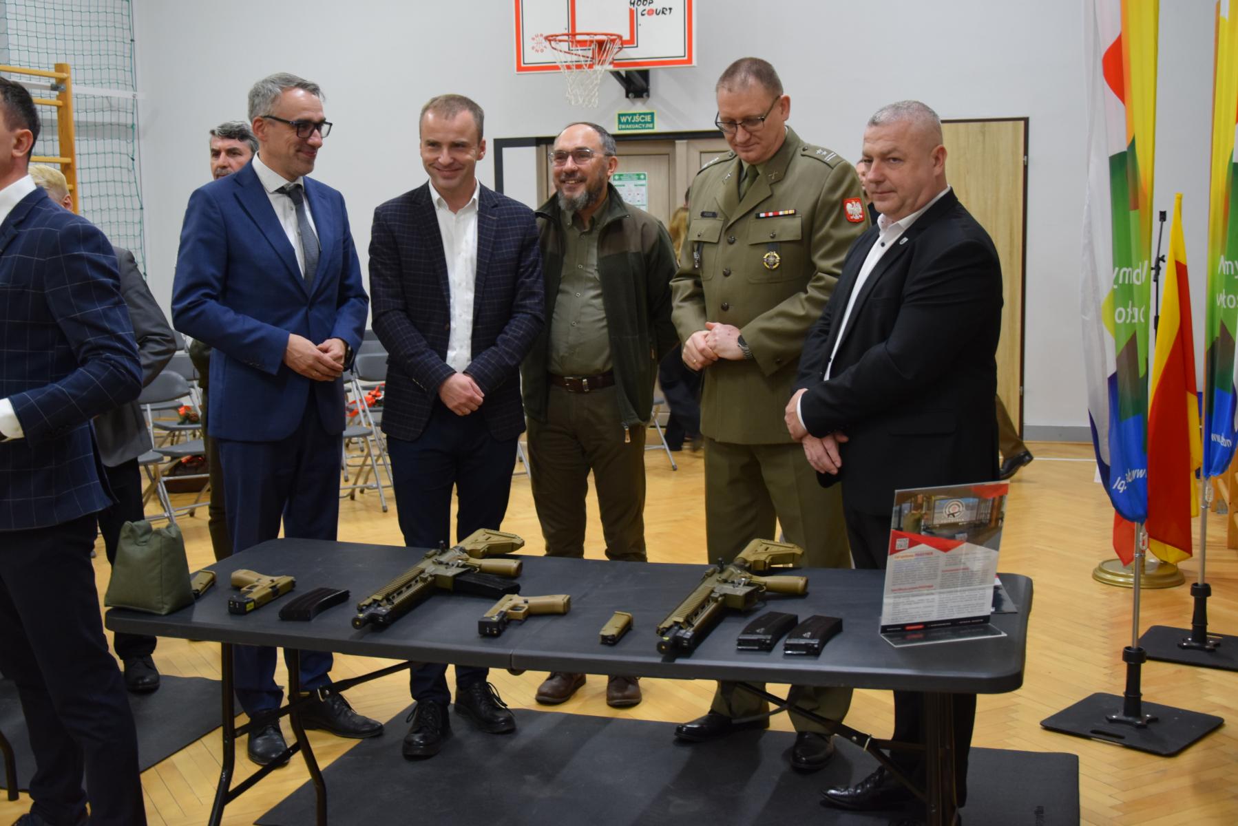 Pieciu mężczyzna stoi przy stoliku z replikami broni