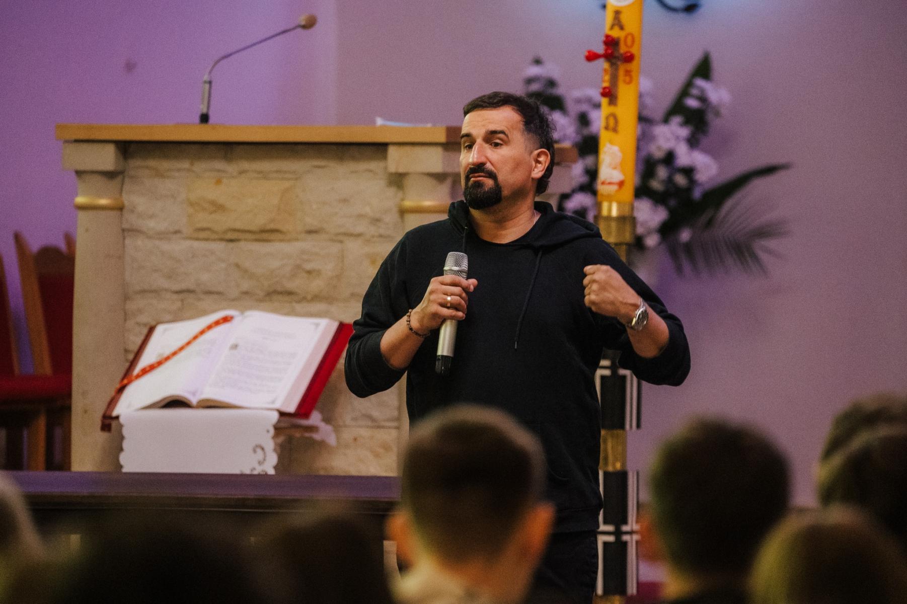 Michał Koterski stoi z mikrofonem w tle świeca