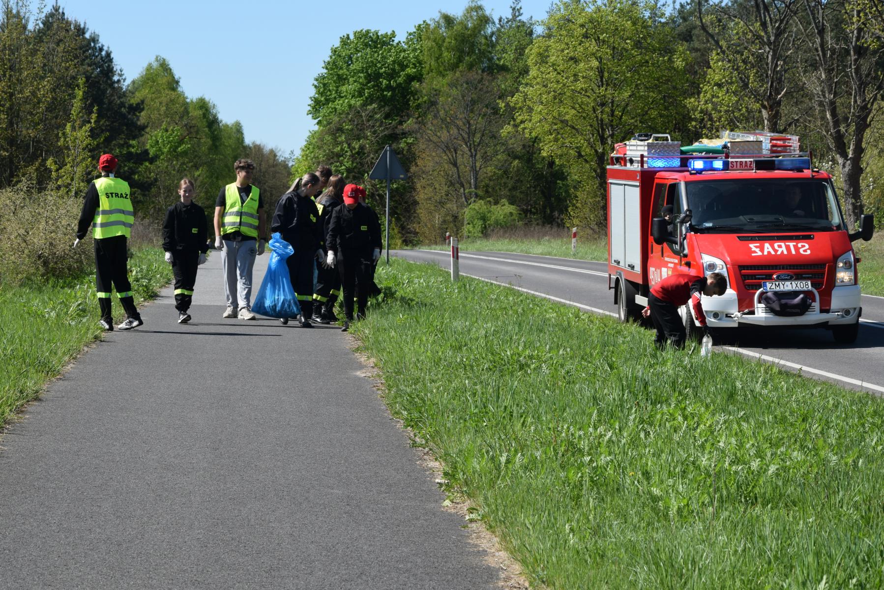 Młodzież idzie z workami, obok busik strażacki