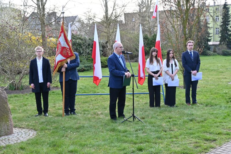Adam Kaczmarczyk stoi przy mikrofonie. w tle flagi Polski