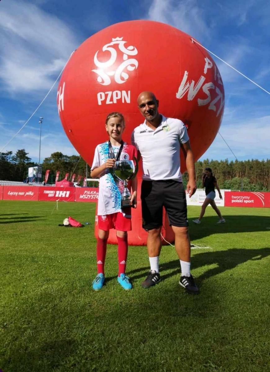 Zawodniczka z trenerem stoją na murawie, w tle duży czerowny balon z logiem PZPN