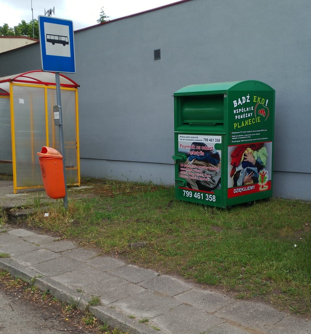 Zielony pojemnik na tesktylia, z lewej obok przystanek autobusowy 