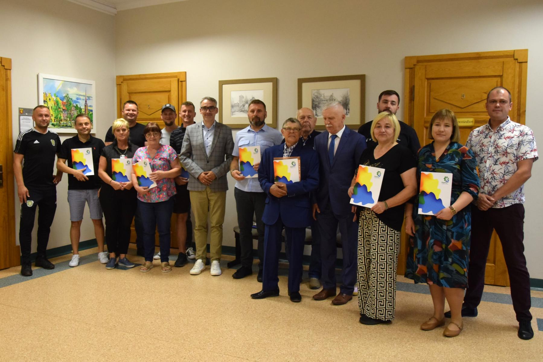 Grupa przedstawicieli organizacji, kobiety i mężczyźni stoją na halu, w tle drzwi, na ścianach obrazy