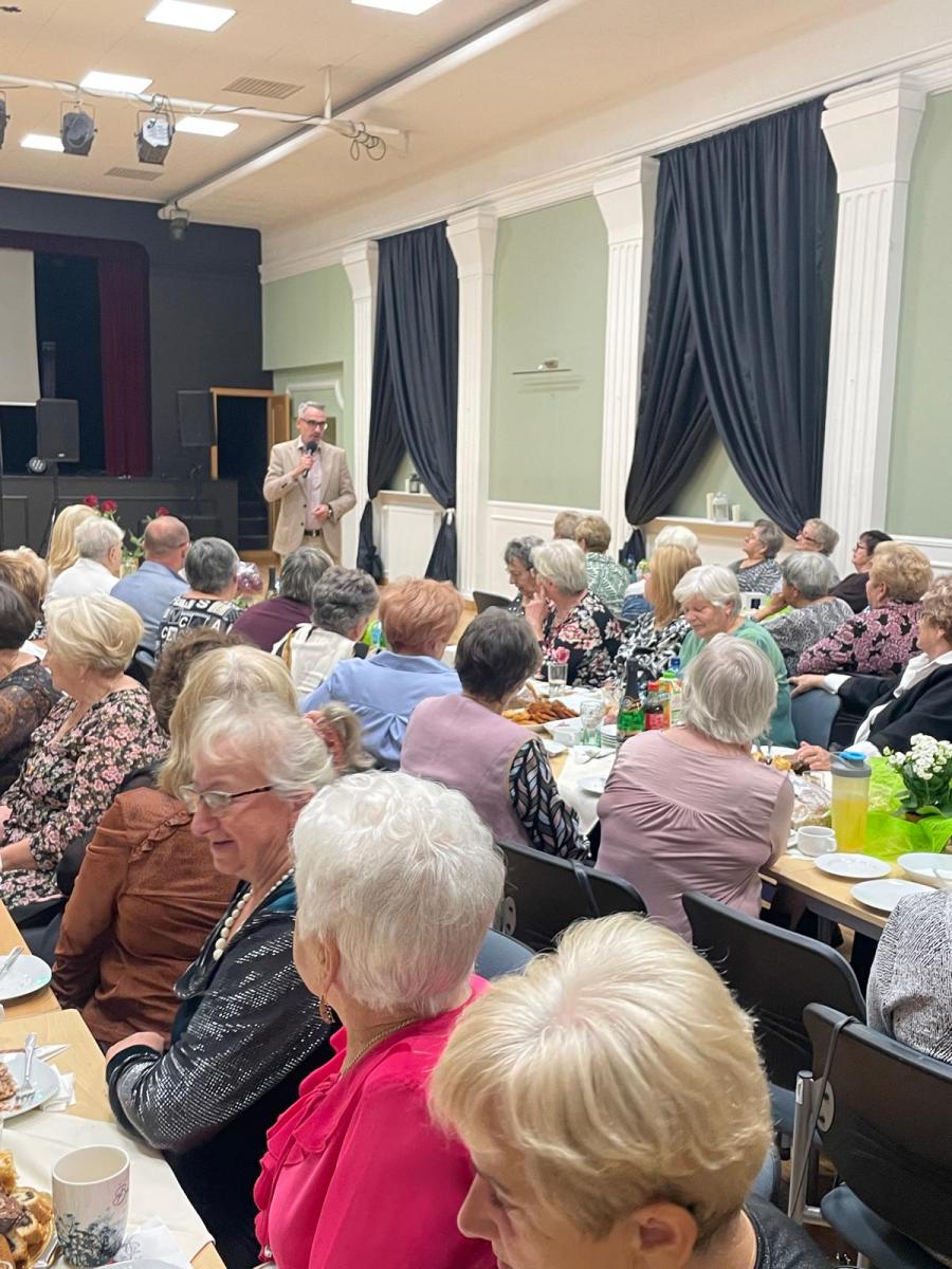 Ludzie siedzą przy stołach w dużej sali, z mikrofonem przed nimi stoi burmistrz Dębna