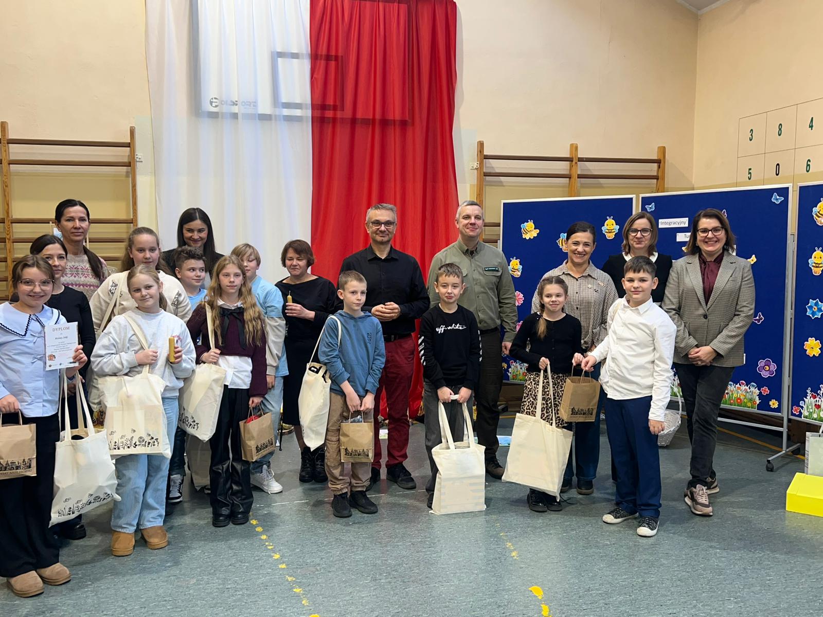 Uczniowie, opiekunowie, członkowie jury, organizatorzy stoją w sali. 