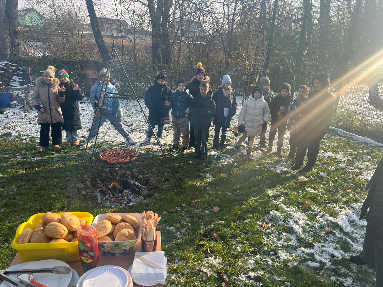 Dzieci na dworze, stoją przed ogniskiem z kiełbaskami na ruszcie