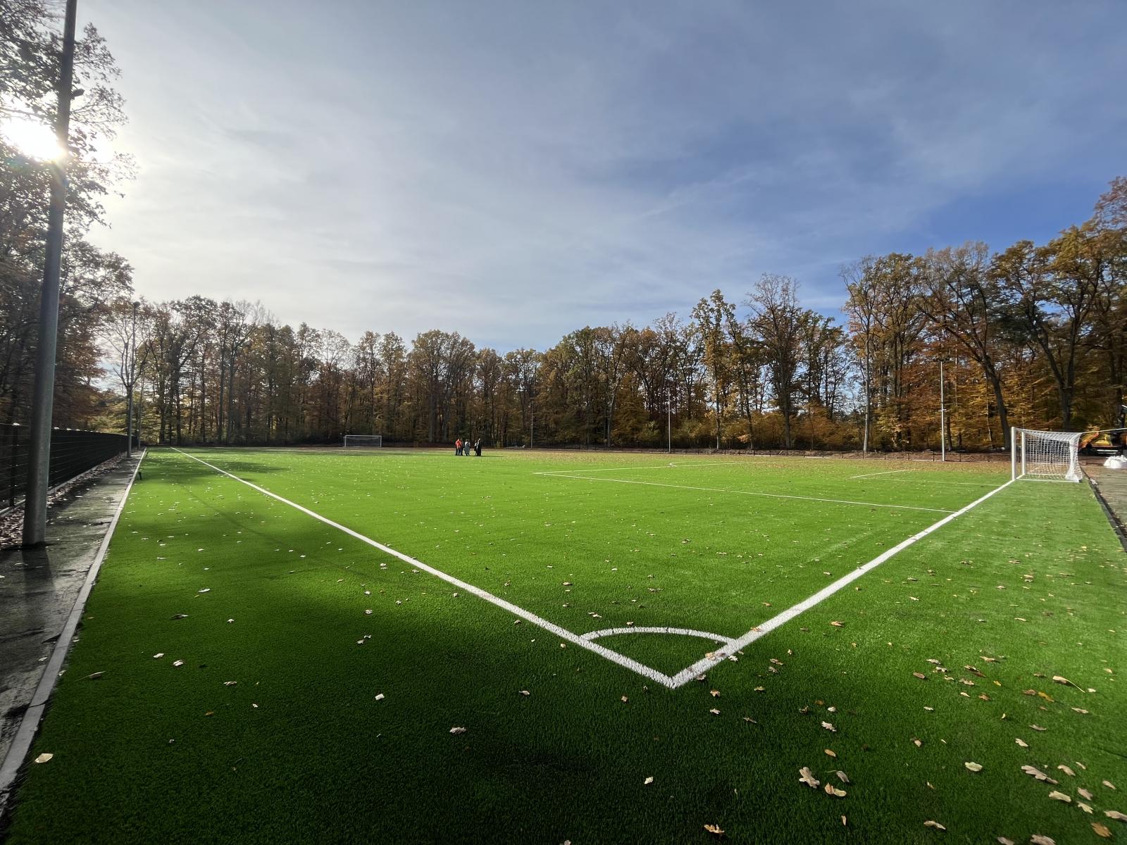 Boisko zielone ze sztuczną trawą., ogrodzone, dookoła drzewa 