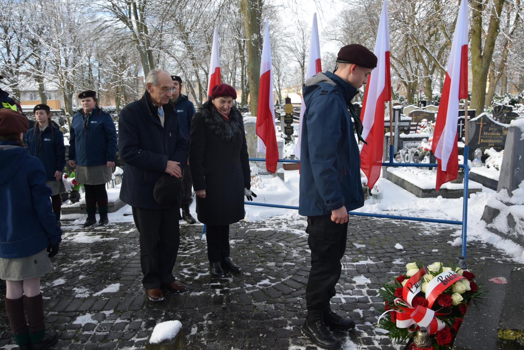 Delegacja kombatnatów i inwalidów wojennych stoi przed grobem, przed nimi stoi druh