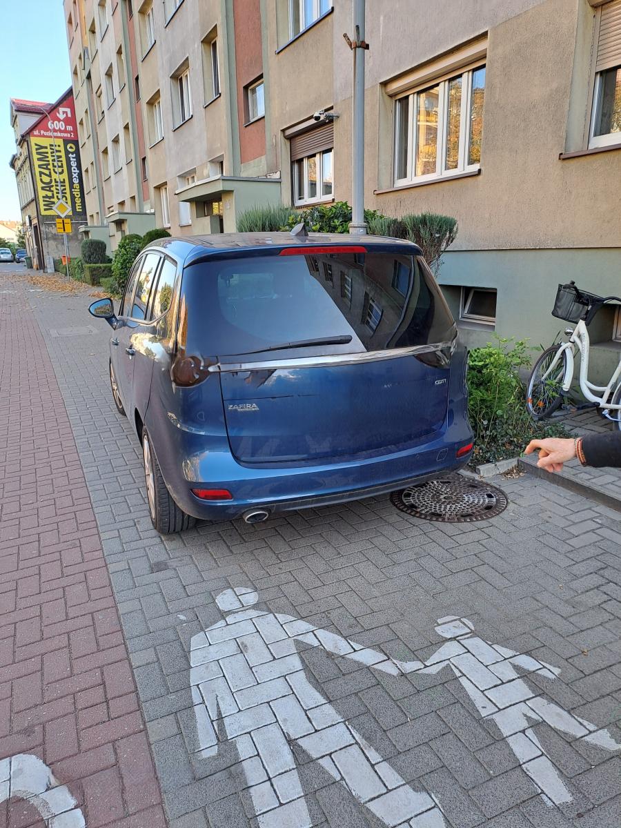 Niebieski samochód osobowy stoi przy bloku na chodniku
