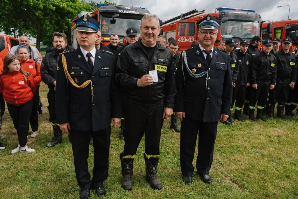 Dwóch strażaków i w środku dorosły ochotnik 