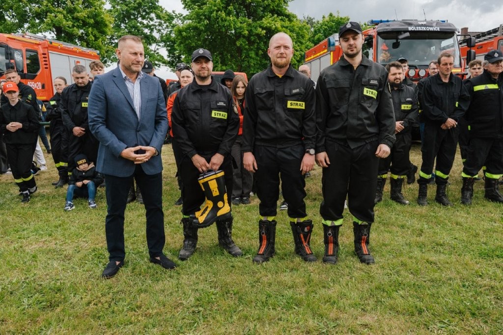od lewej stoja mężczyzna, następnie trzech strażaków, drugi trzyma kalosze w ręce