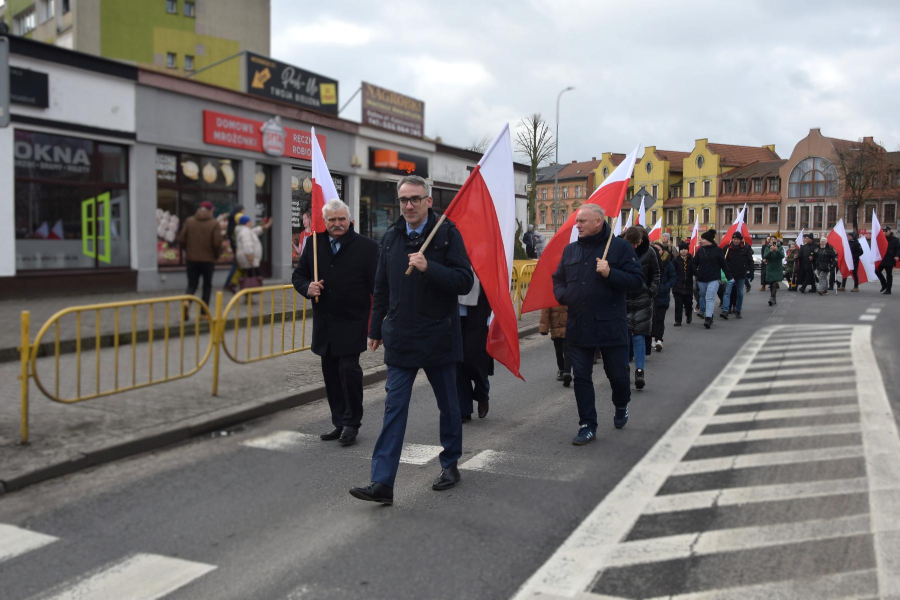 Ludzie idą ulicą, trzymają flagi Polski w dłoniach. na przodzie burmistrz Dębna 