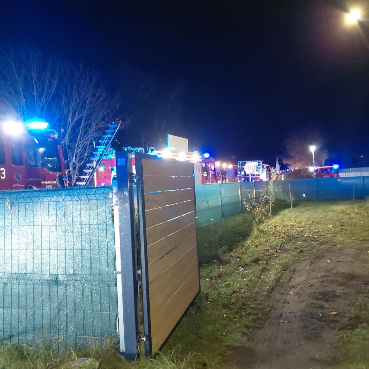 Na zdjeciu noc, widać oswietlone wozy strażackie za płotem