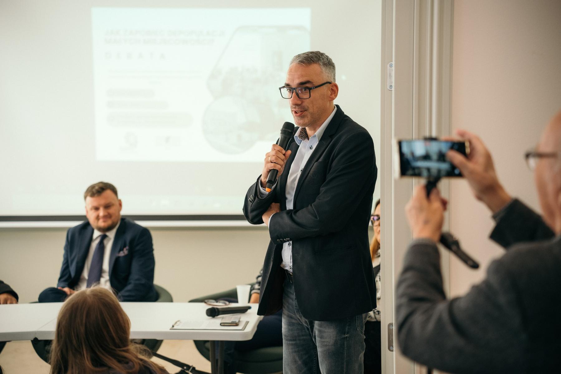 Burmistrz Dębna stoi w sali w ręku trzyma mikrofon