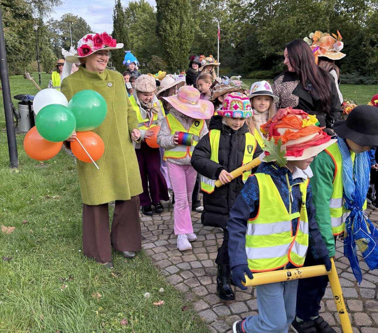 Dzeci na głowei z kolorymi kapeluszami, obok sekretarz gminy trzyma kolorowe balony 
