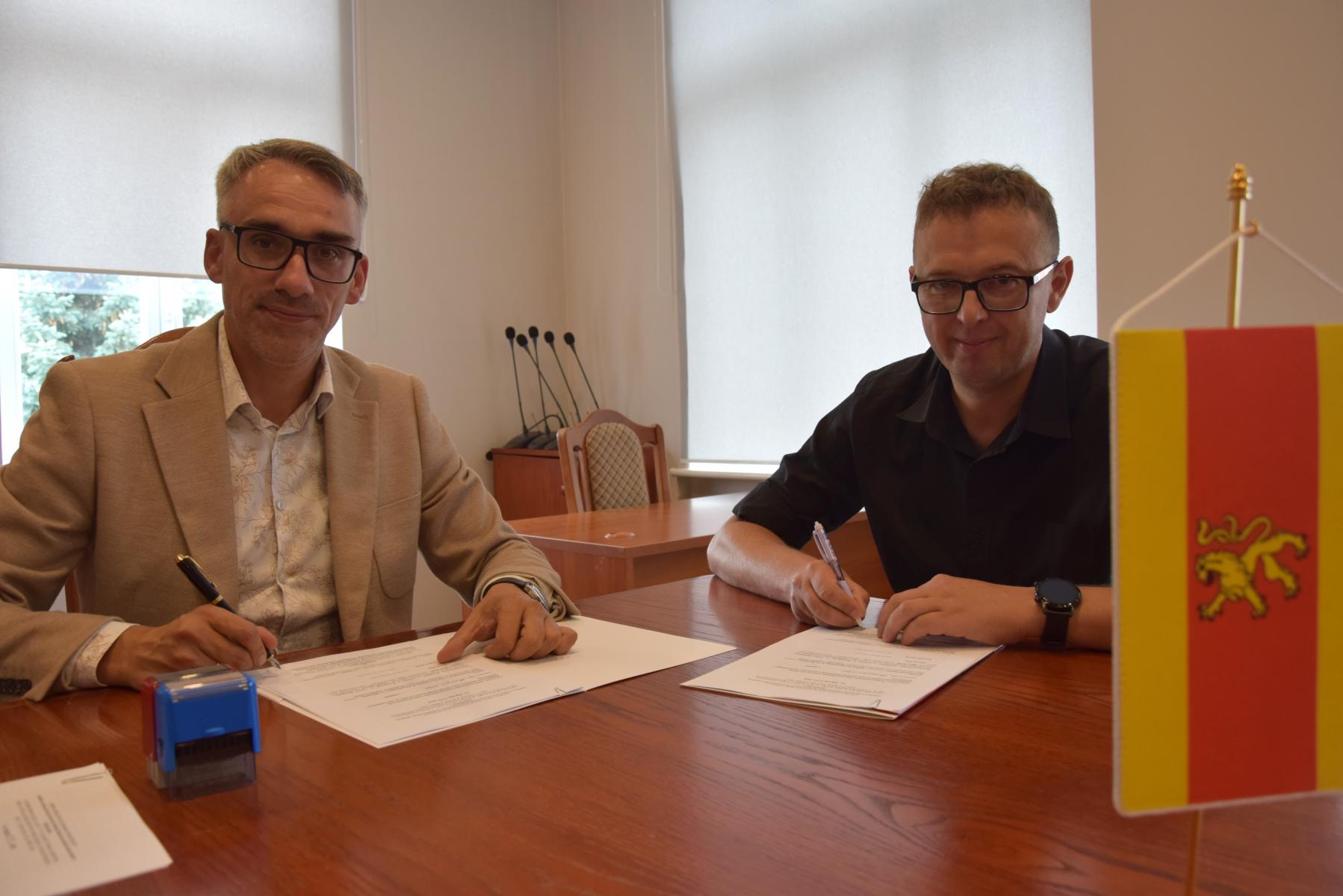 Burmistrz Dębna i Marcin Pleń siedzą przy stole w sali. Na stole leżą dokumenty