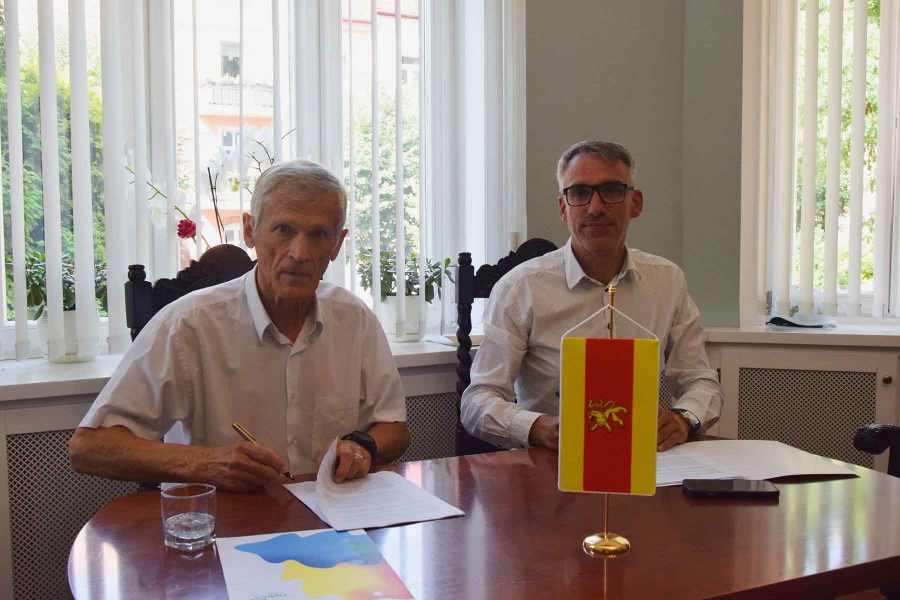 Dwóch mężczyzn siedzi przy stole, proporczyk Gmina Debno stoi na stole 