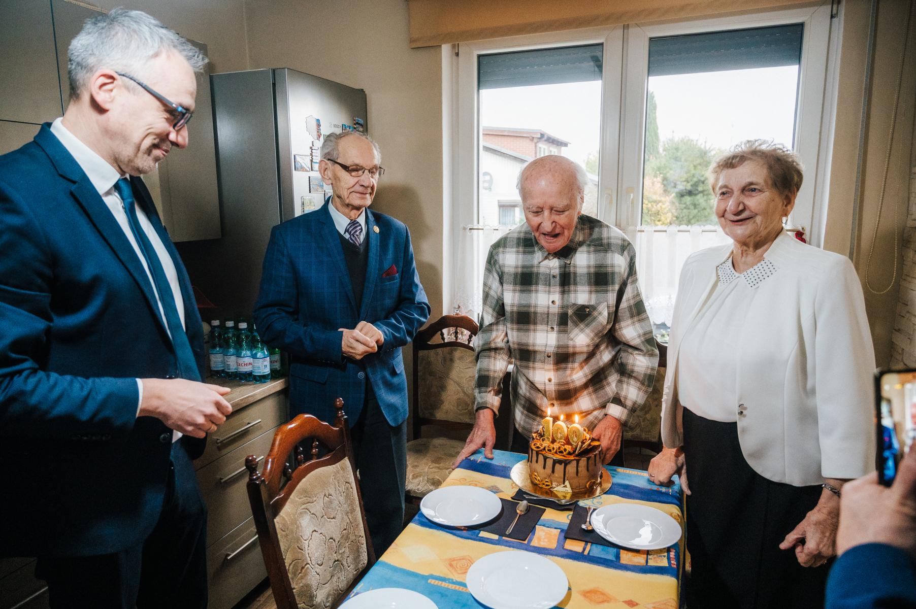 Goście stoją wraz z jubilatem, na stole stoi tort