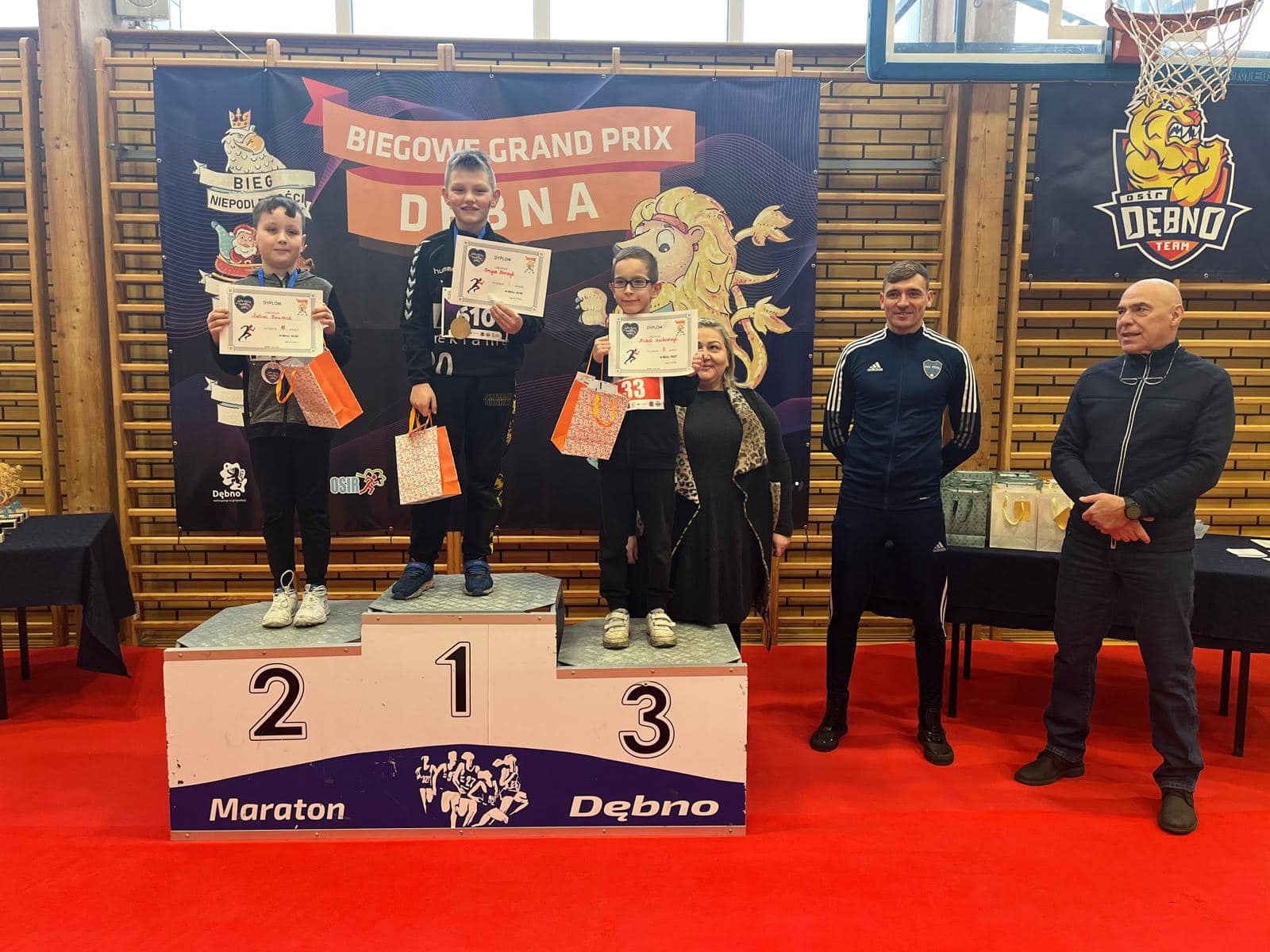 Trzech chłopców stoi na podium, po prawej stoi kobieta i dwóch mężczyzn