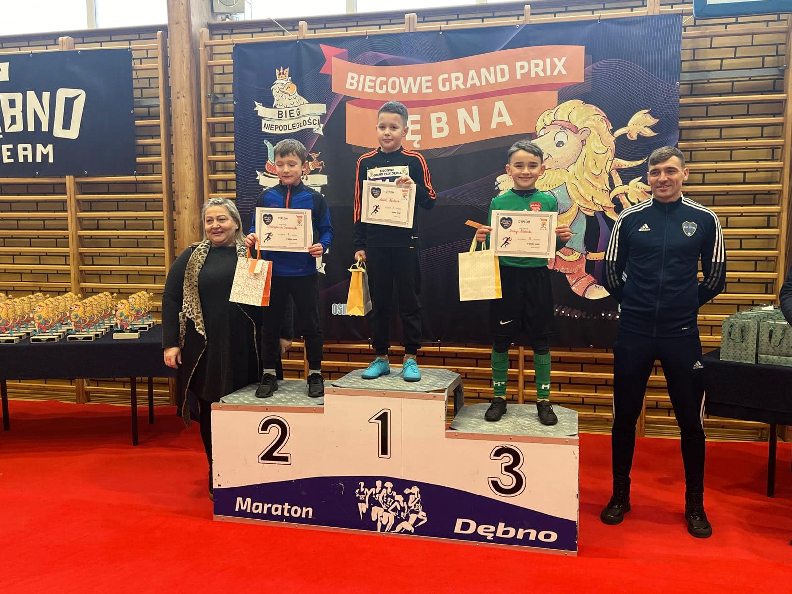 Trzech chłopców stoi na podium, obok po lewej stoi kobieta, po prawej mężczyzna   