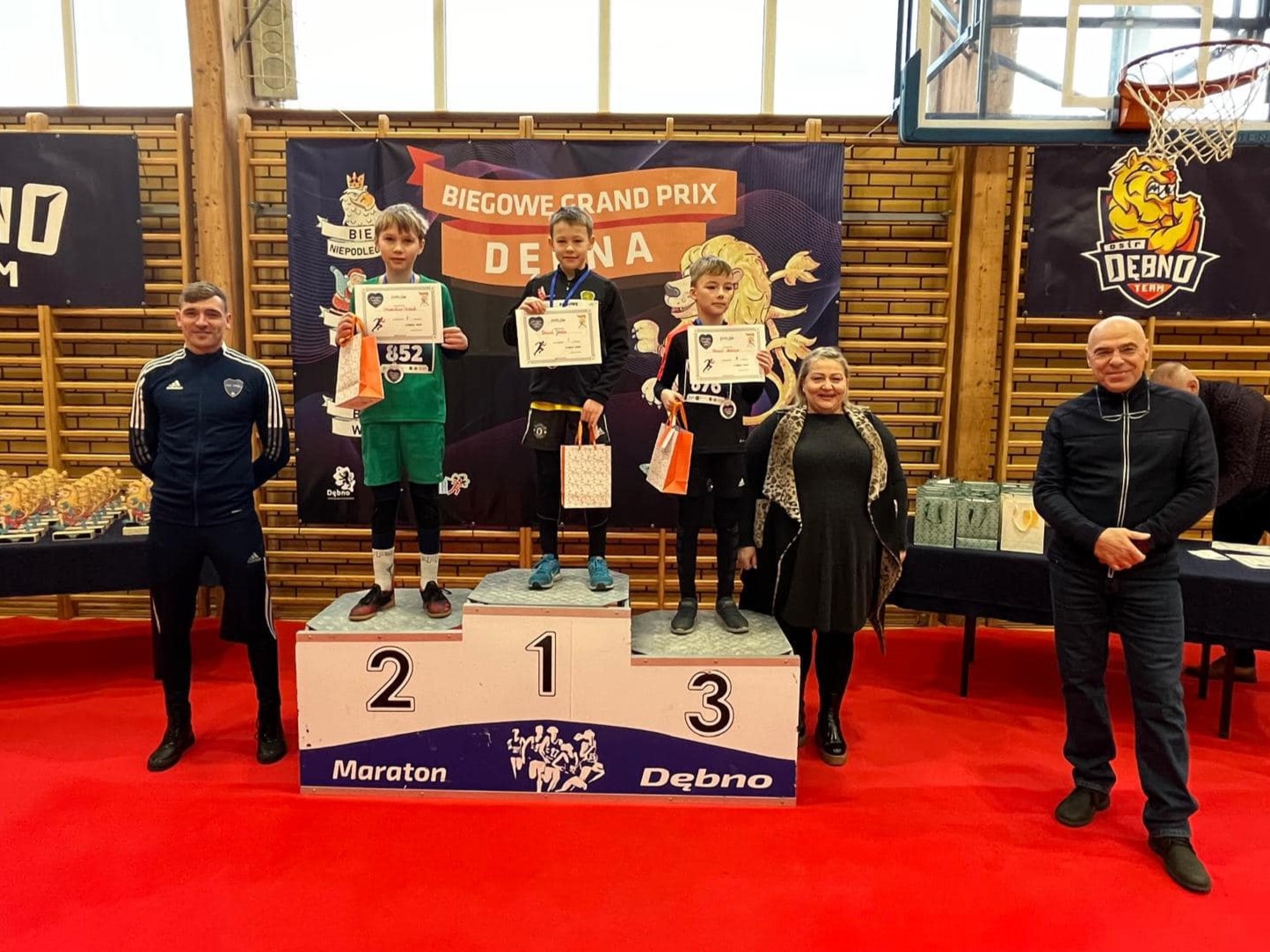 Trzech chłopców stoi na podium, po prawej stoi kobieta, po lewej mężczyzna