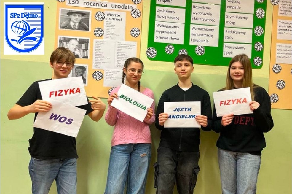 Czworo uczniów stoi na holu. w rekach trzymają kartki z nazwami przedmiotów 