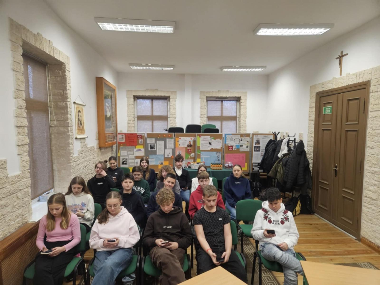 Uczestnicy konkurus siedzą na krzesłach, w dłoniach trzymją telefony