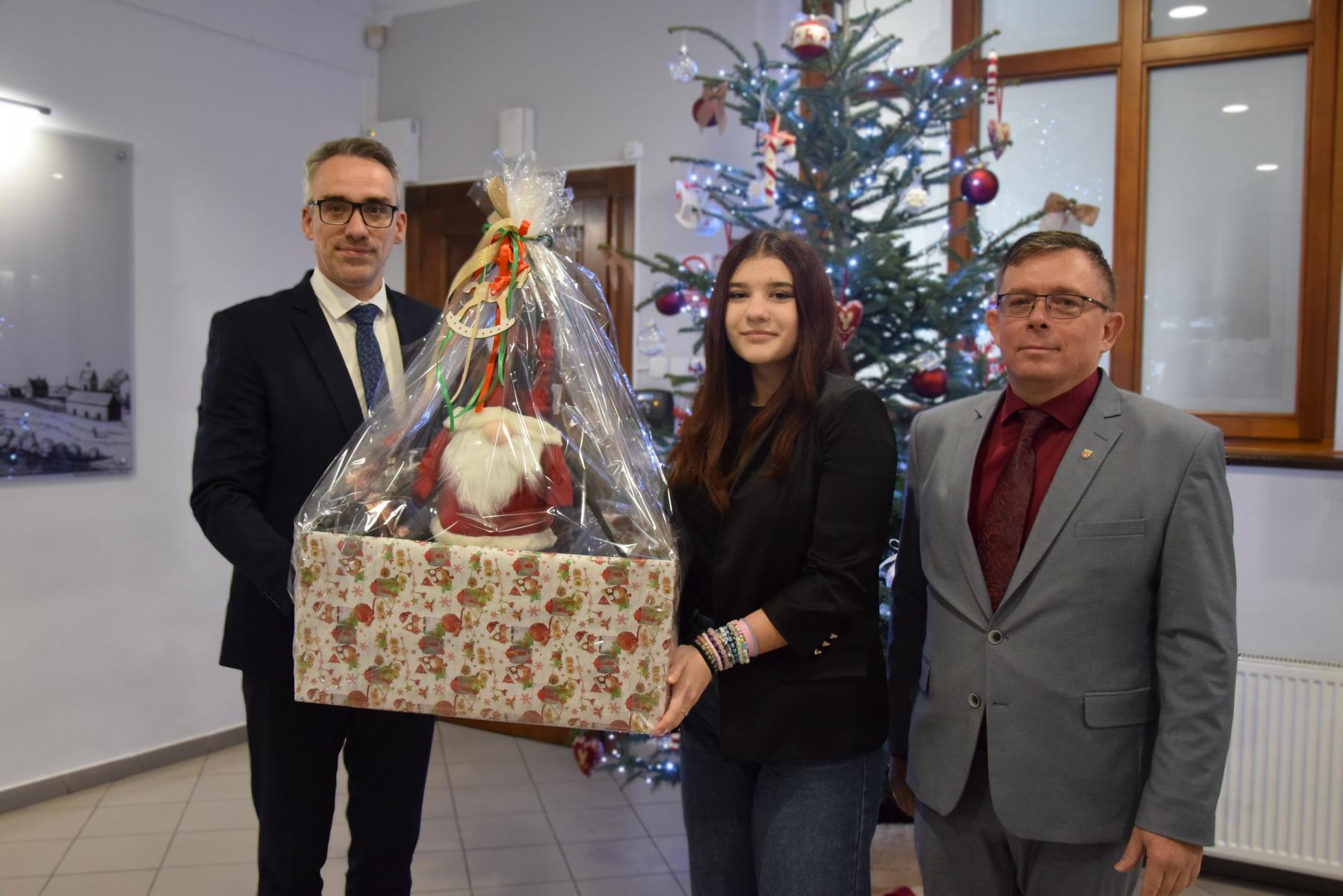 od leej burmistrz, młoda dziewczyna trzymają prezent w rękach, przewodniczący rady,. W tle choinka 