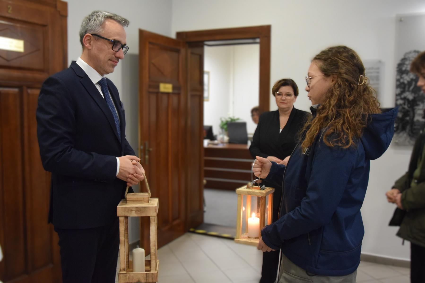 Burmistrz Dębna trzyma latarenkę, na przeciwko stoi harcerka z latarenką 