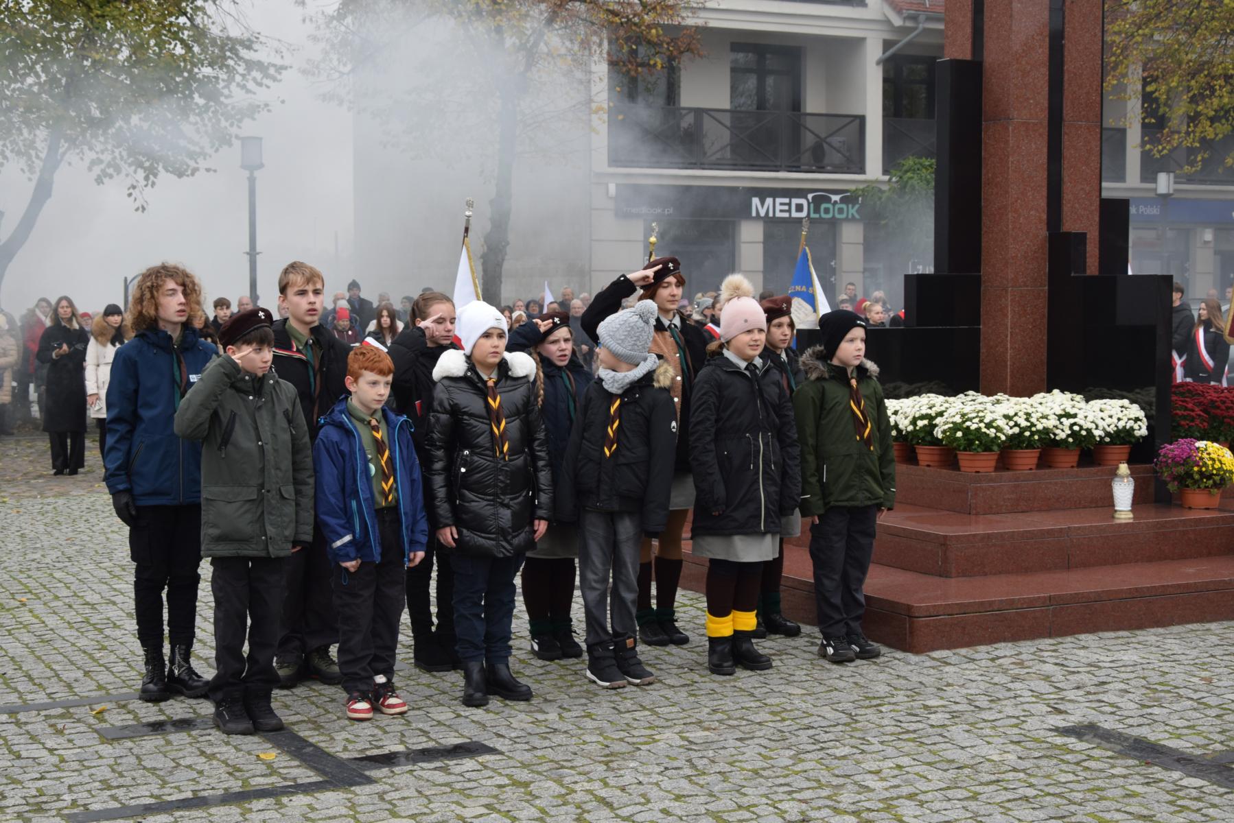 Młodzi harcerze i harcerki stoją przy pomniku