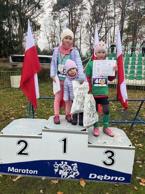 Dwie dziewczynki stoją na podium. Z tyłu powiewają biało-czerwone flagi 