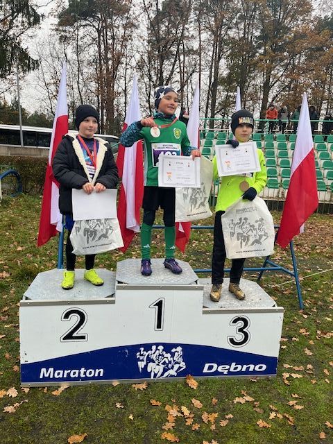 trzech chłopców stoi na podium. Z tyłu powiewają biało-czerowne flagi