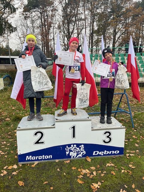 trzy dziewczynki stoją na podium. Z tyłu powiewają biało-czerowne flagi