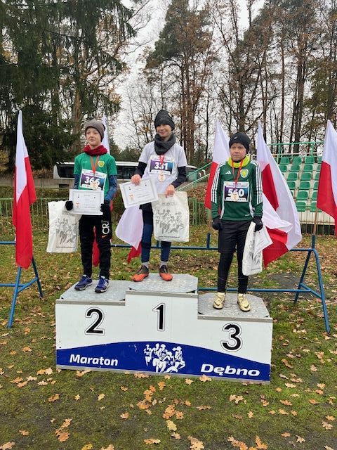 trzech chłopców stoi na podium. Z tyłu powiewają biało-czerowne flagi