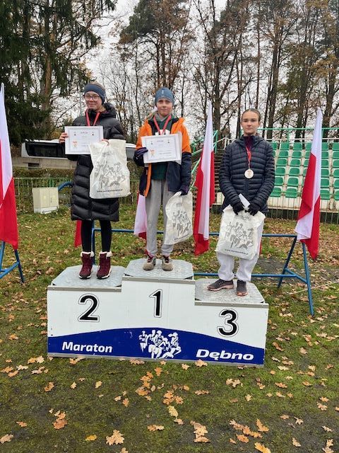 trzy dziewczynki stoją na podium. Z tyłu powiewają biało-czerowne flagi