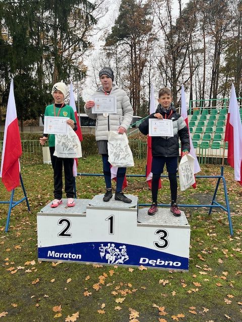 trzech chłopców stoi na podium. Z tyłu powiewają biało-czerowne flagi
