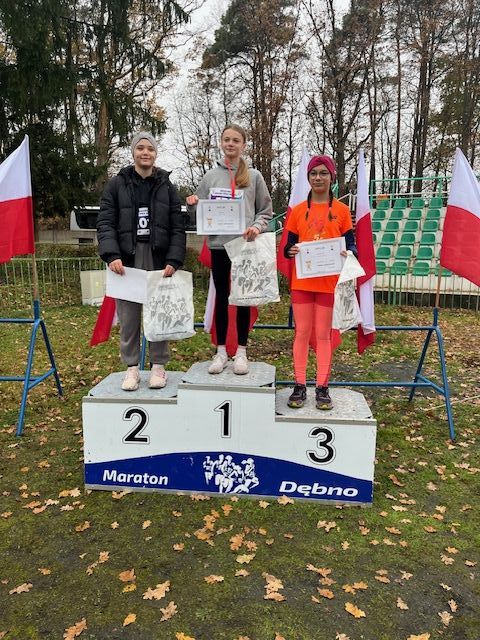 trzy dziewczyny stoją na podium. Z tyłu powiewają biało-czerowne flagi