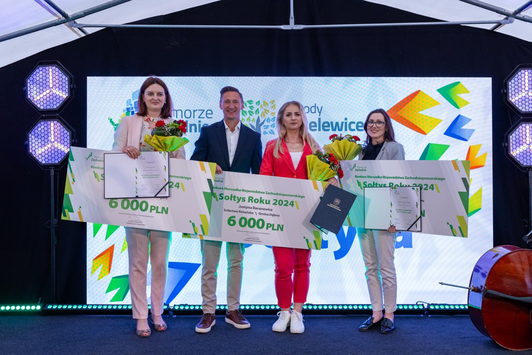 Na scenie stoją od lewej: kobieta, marszałek O. Geblewicz, Justyna Baranowicz, kobieta. W rękach trzymają czeki z kwotą 6000 PLN