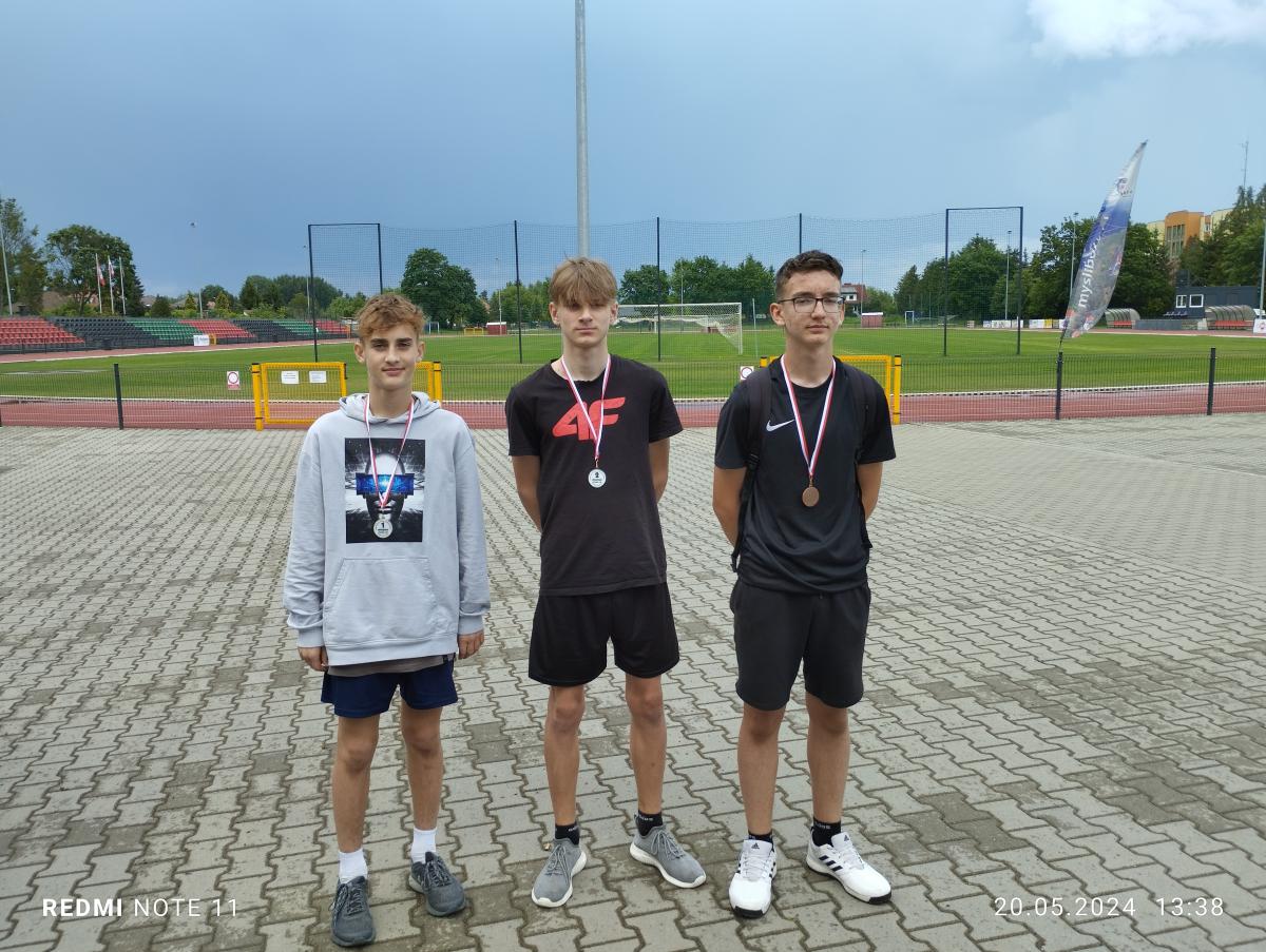 Trzech chłopców z medaliami na szyi. W tle stadion